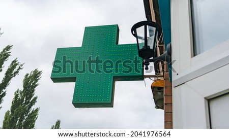 Green cross next to a pharmacy on a cloudy sky background