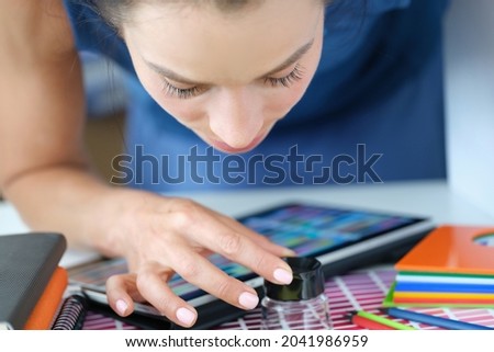 Woman designer looking through magnifying glass at color samples on paper palette Royalty-Free Stock Photo #2041986959