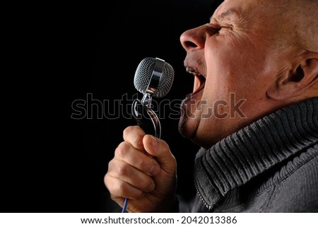 adult man emotionally screaming, singing into studio microphone on black background, music recording concept, blogger equipment