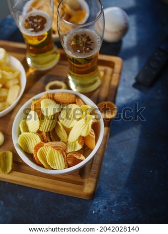 Two glasses of light beer, potato chips, onion snacks and a TV remote on a blue background. Low angle view. Watching your favorite TV shows with friends, with your family, beer, cold snacks.