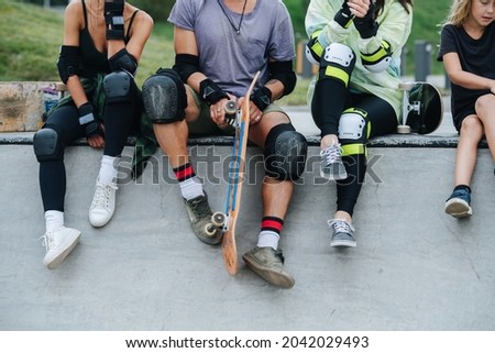 No head image of skaters chilling on the deck at skatepark, hanging their legs in knee pads. Frontal view.