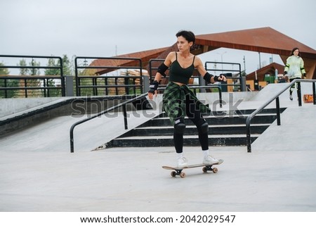 Dinamic image of a confident woman skater with short hair riding on her board on concrete paving at skatepark. She wears some protective gear.