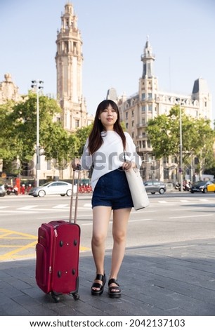 Smiling young tourist chinese girl taking a walk in the town with a travel bag. High quality photo