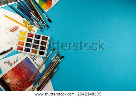 Watercolor paints and brushes.  Color palette. Drawing blue background. Art created. Copy space. Paints and brush. Watercolor illustrations. Sketches. Artist's workplace. Draw paint. Craft home hobby 