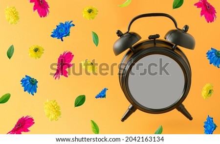 Old brown clock with blank space and colorful spring flowers flying on a orange background. Positive news, thinking and energy concept. Optimistic future, mood and atitude. Limited time offer concept.