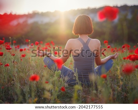 A beautiful woman meditates on a poppy field at sunset. Wellness well-being happiness concept. Royalty-Free Stock Photo #2042177555