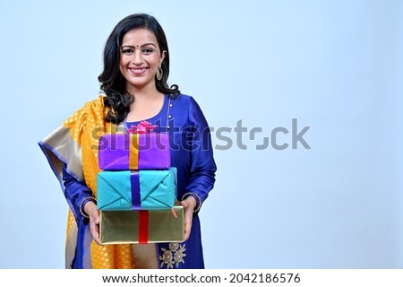 Beautiful hindu women in Tradional wear holding gift boxes in hand in greeting pose, studio shot Royalty-Free Stock Photo #2042186576