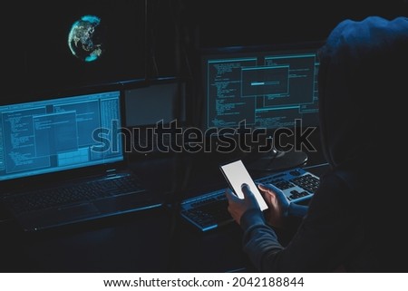 Overhead hacker in hood working at laptop and mobile phone typing text in dark room, An anonymous hacker uses malware with mobile phone to hack password, personal data steals money from bank. cyber Royalty-Free Stock Photo #2042188844