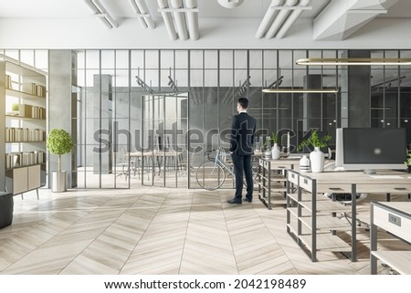 Businessperson standing in modern coworking office interior with bright city view and wooden flooring. Design and workplace style concept
