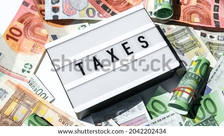 Lightbox board with word TAXES in black letters around Euro banknotes. Tax payment and filing concept. Money, Business, finance, investment, saving and corruption. Cash bill