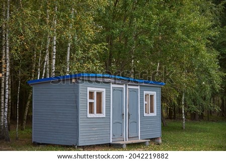 A small gray summer house stands in a clearing against the background of birch trees.