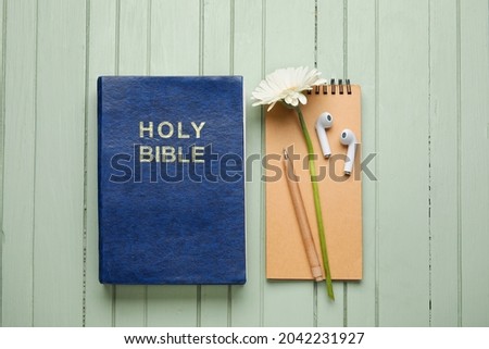 Holy Bible, earphones and flower on color wooden background