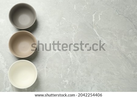 Stylish empty ceramic bowls on grey table, flat lay and space for text. Cooking utensils