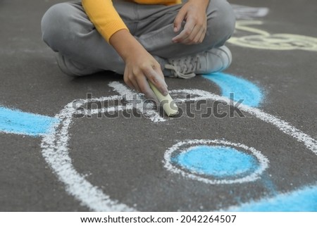 Child drawing rocket with chalk on asphalt, closeup