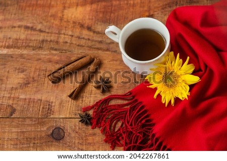 Winter, warm atmosphere. Cup of hot black tea with red scarf, cinnamon sticks and sunflower on wooden background. Winter evening. Flat lay, layout, place for text, post card, high resolution