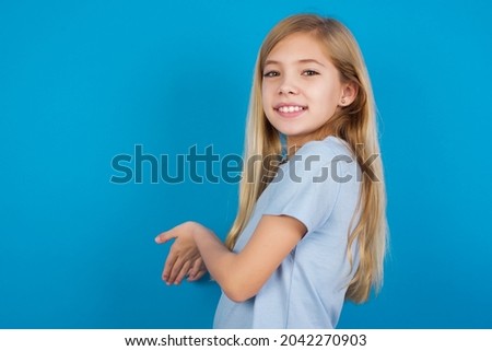 beautiful caucasian little girl wearing blue T-shirt over blue background Inviting to enter smiling natural with open hands. Welcome sign.