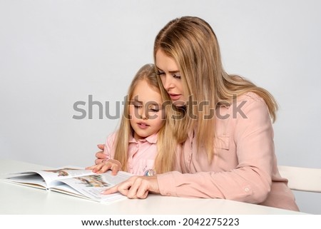 Studio shot of mom teaching little daughter to write and read