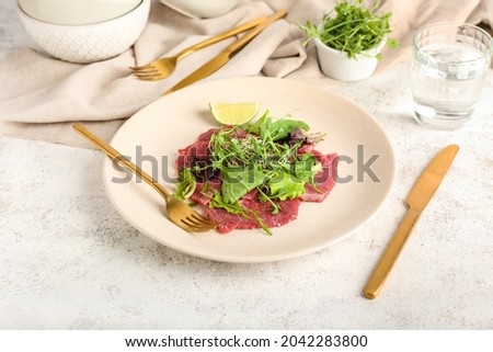 Plate with tasty veal carpaccio, glass of water and fresh sprouts on light background