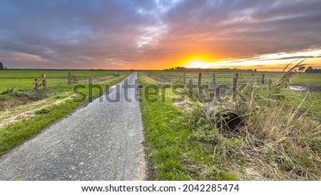 Sunset over rural road in lowland meadow farmland in Sint Jansklooster, Overijssel, Netherlands.