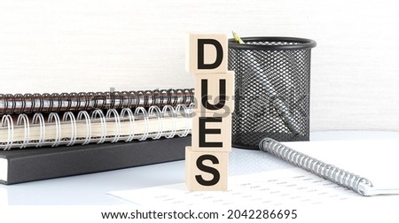 DUES text on the wooden block with notebooks on white background