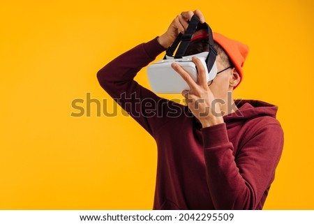 happy man puts on virtual reality glasses, in an orange hat and a red sweatshirt, on a yellow background, concept: future, 3d, 4d, glasses