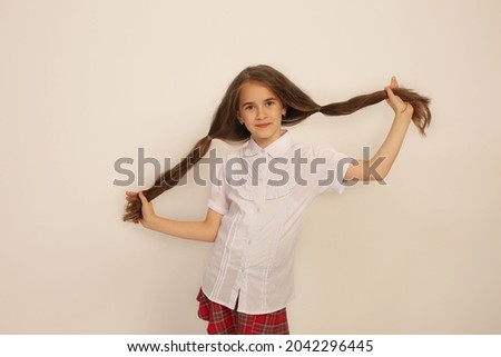 a schoolgirl girl in a white shirt and a plaid skirt holds herself by long tails of hair