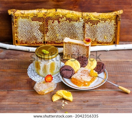 Rustic still life with beekeeping products: honey combs in a glass jar, wild honey in a honeycomb frame on a birch branch, a cookies and cut combs on a plate, on a wooden background