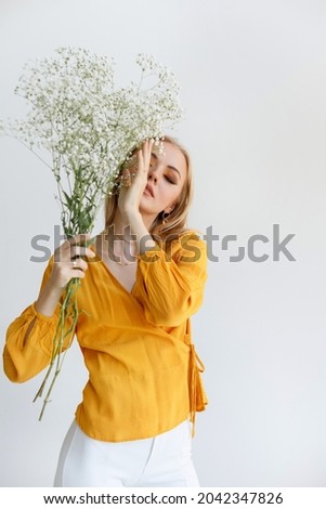 a young blonde with dry flowers covers her face with her hand. fashionable makeup