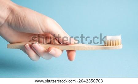 Hand holding bamboo toothbrush on blue. Holding wooden eco toothbrush. Natural toothpaste on a bamboo toothbrush Royalty-Free Stock Photo #2042350703