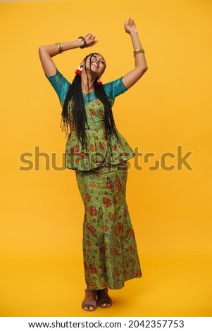 Black mid woman with  pigtails smiling while dancing on camera isolated over yellow background