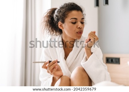 Smiling young african woman in bathrobe sitting on a bed filing her nails in the bedroom