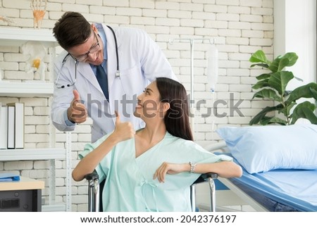 Caucasian Male Doctor visits and talks to Asian woman patient on wheelchair smile confident friendly in clinic. people treatment of diagnosis health check medical consultation at hospital - Concept.