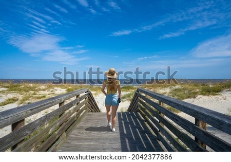 Woman enjoying time on the beach. Girl walking on wooden path over dunes at a beach leading to the ocean. Oceanview Beach Park, Jekyll Island, Georgia, USA. Royalty-Free Stock Photo #2042377886