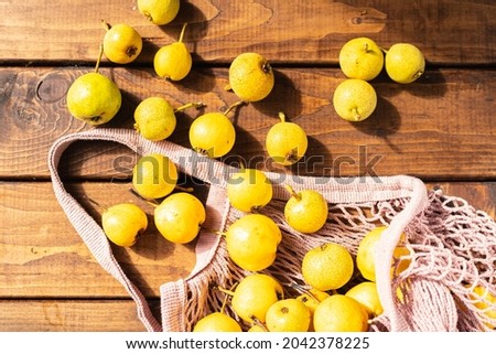 a lot of yellow pears spill out of a wicker mesh bag on a wooden table