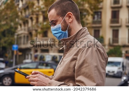 An actively engaged man texting while outside in the street and wearing a mask