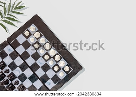 Chess game. Chess composition with a chess board with placed pieces and palm leaves on a blue background with place for text. Banner for chess competition. Flat lay