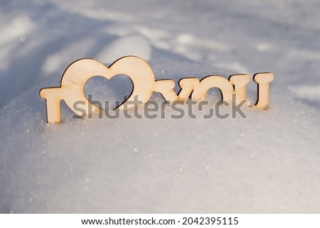 Wooden inscription I love you stands in snowdrift. Sunny winter day and sparkling snow. Horizontal photo, romantic concept