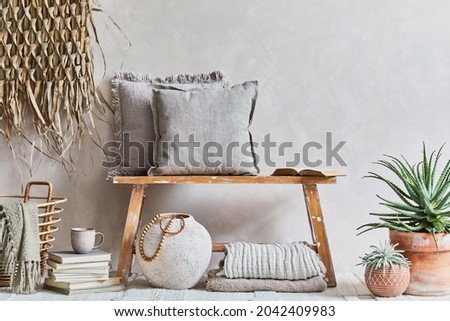 Stylish composition of cozy living room interior with copy space, bench in retro style, clay vase, crockery, straw wall decoration and textiles. Rustic inspiration. Summer vibes. Beige wall. Template.