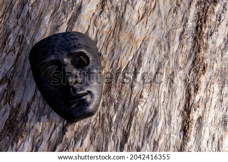 Selective focus black plastic mask placed on a beautifully patterned stone. give a strong feeling and has dark powers concept of the dark side of man There is space for text.