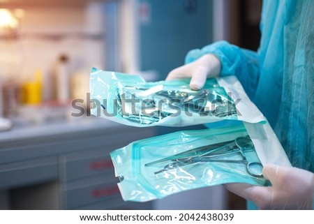 Close up of dentist hands in white sterile gloves holding dental tools for surgical use packed in a protective foil at dental office Royalty-Free Stock Photo #2042438039