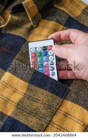 multi colored remote. puts the multi colored remote in her shirt pocket. rgb. close up.