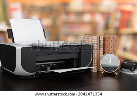 Compact home printer on desk with books against blurred background
