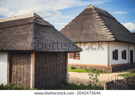 A traditional old country house with a thatched roof and a barn with an intertwining pergola. Traditional view of the village courtyard. Royalty-Free Stock Photo #2042473646
