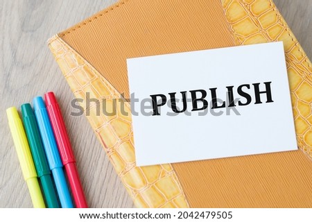 notepad on which the card is with text PUBLISH on the on the table next to colored markers