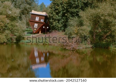 Picturesque fairy view. A house turned upside down, a fallen tree and their reflections in the water surface of the river. 