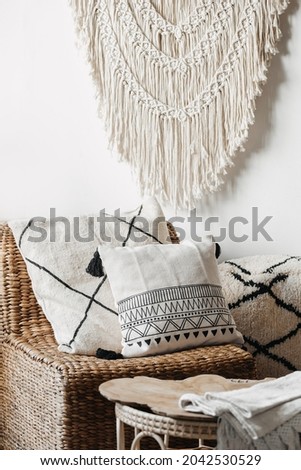 Vertical view of cozy living room interior in bali or indonesian style, with home decor, wicker furniture, armchair with cushions and macrame on white wall Royalty-Free Stock Photo #2042530529