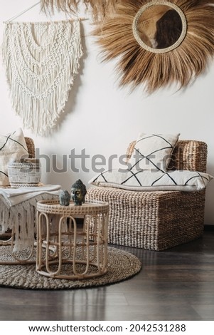 Natural material furniture and macrame on white wall in living room interior in bali or indonesian style. Vertical view of comfortable armchair with cushions near bamboo coffee table with home decor Royalty-Free Stock Photo #2042531288