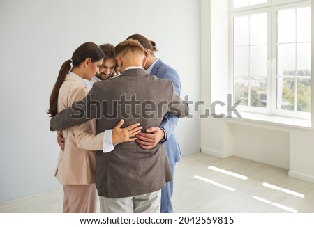 Business, respect, cohesion and teamwork. Group of business people standing in a close circle in a bright empty room and hugging each other. Colleagues support each other at the company's seminar. Royalty-Free Stock Photo #2042559815