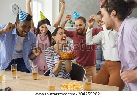 Hooray, you turned twenty today. Diverse multiracial group of excited friends giving a cake to a happy young woman at her birthday party at home. Young woman in her 20s getting presents and having fun