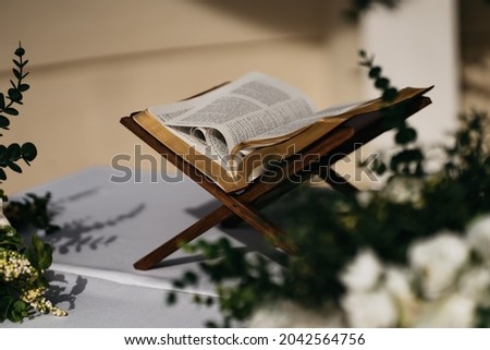 View of a Bible surrounded by flowers standing on a wooden stand during wedding ceremony